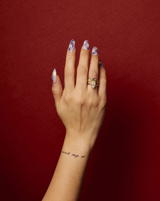 hand wearing the element 2 ring on ring finger stacked with an engraved gold band on red background