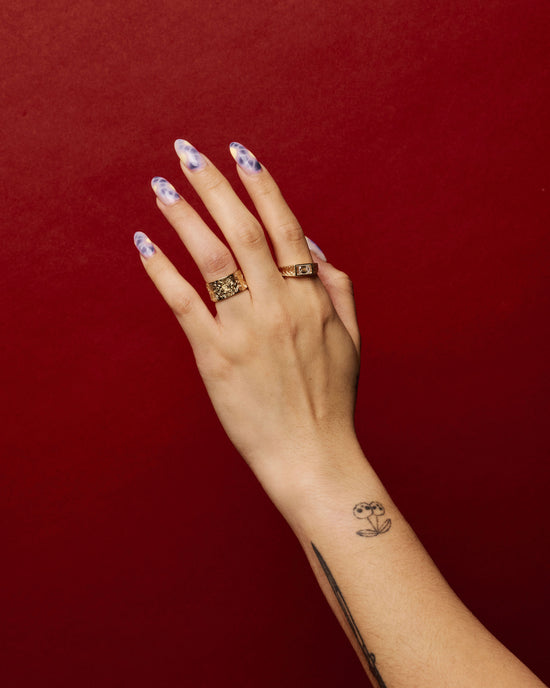 hand wearing the element 6 ring on ring finger with another gold diamond band on pointer finger over a red background