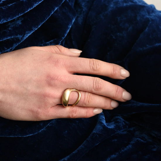 close up of model wearing the brass drip double band ring on their ring finger with blue velvet background