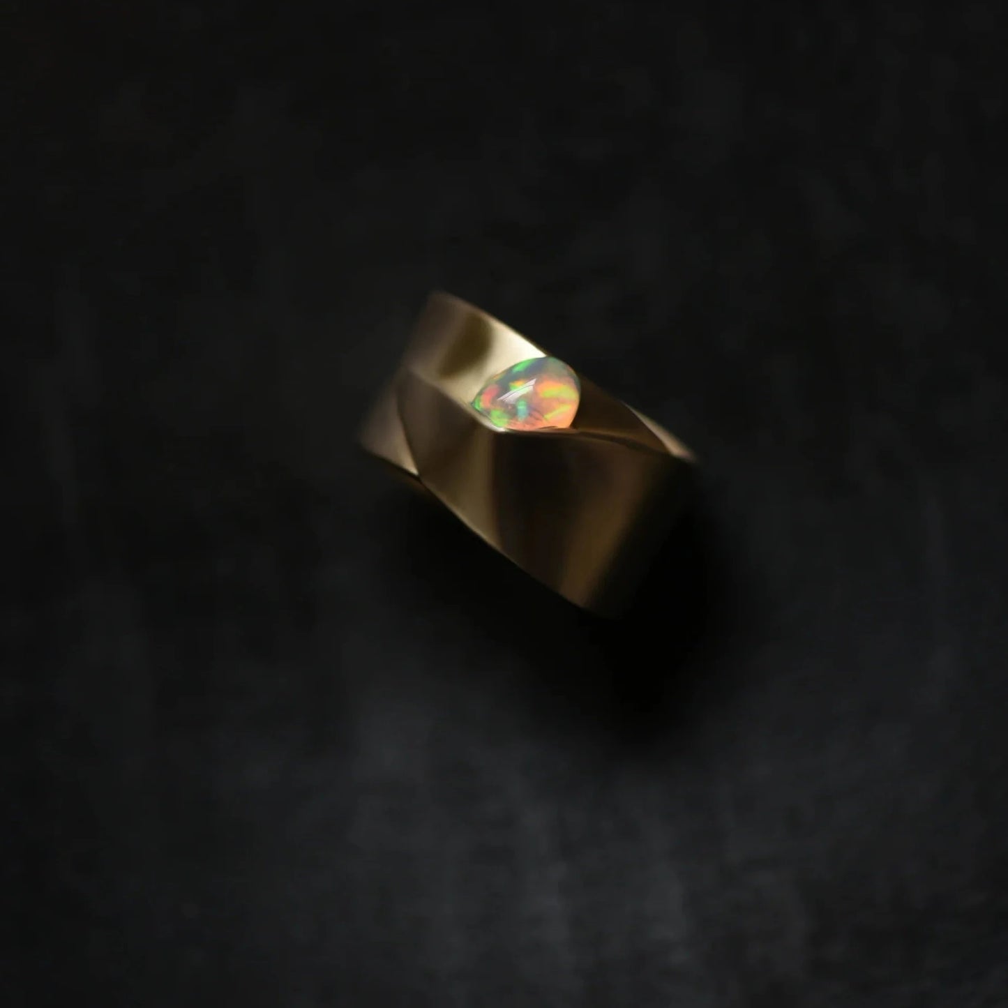 a organic shaped wide brass band with a partially hidden oval opal on a gray background