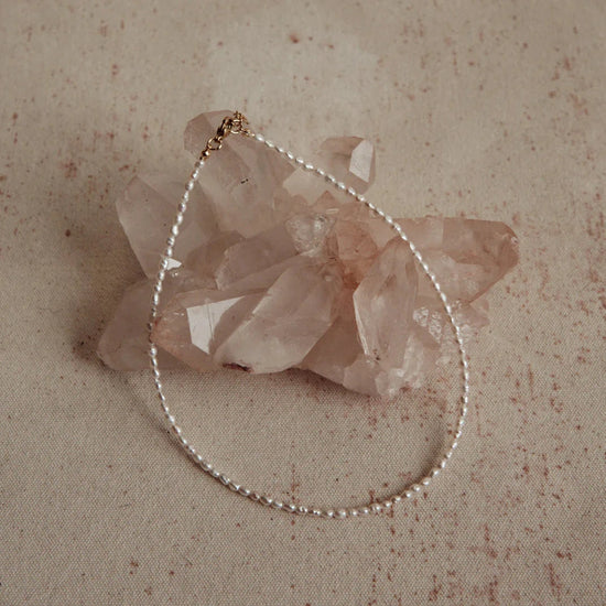 thin pearl seed necklace sitting on a pink crystal