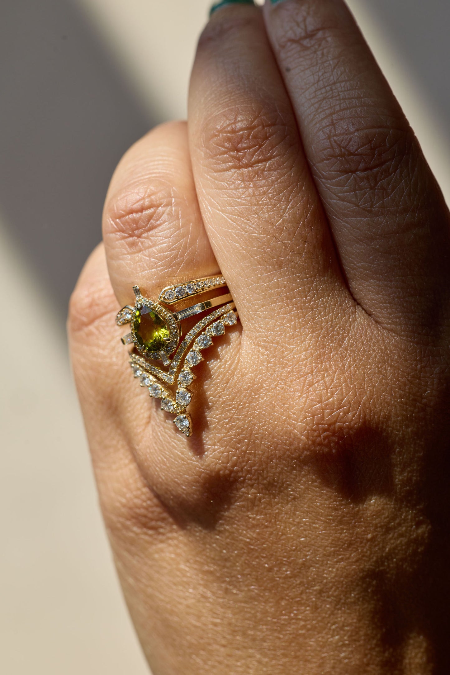 Close-up of a hand wearing a gold ring with a yellow gemstone on a neutral background