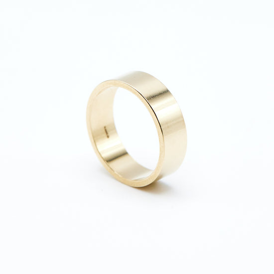 angled view of the yellow gold flat wedding band on a white background