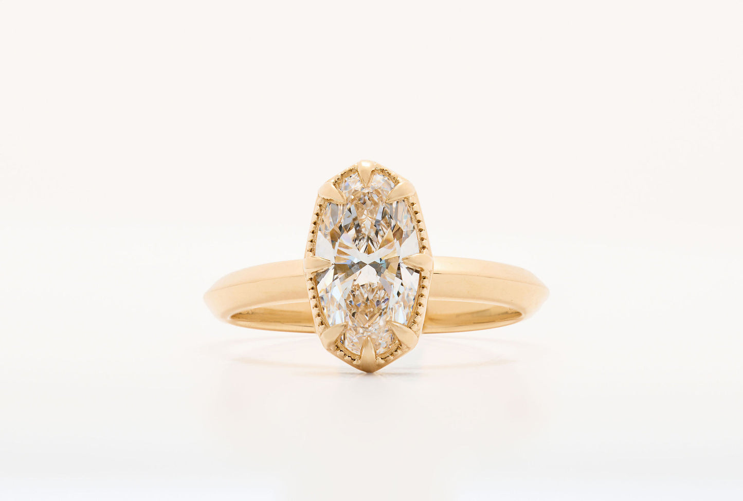 element ring 2, an oval diamond solitaire with 8 claw prongs and milgrain border on a knife edge band in yellow gold, close up on a white background