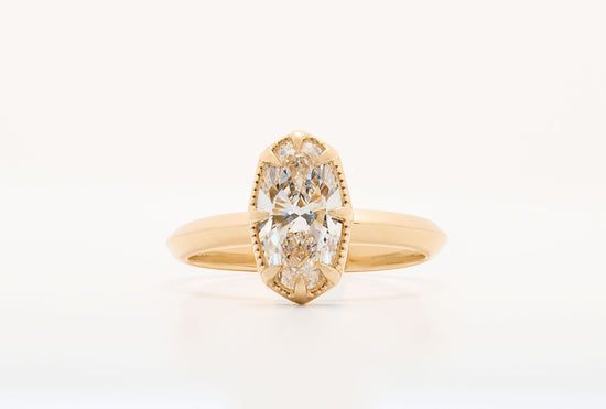 element ring 2, an oval diamond solitaire with 8 claw prongs and milgrain border on a knife edge band in yellow gold, close up on a white background