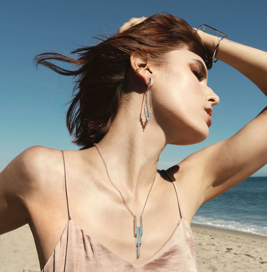 White gold dangle earrings on a model with the sky, ocean, and sand in the background