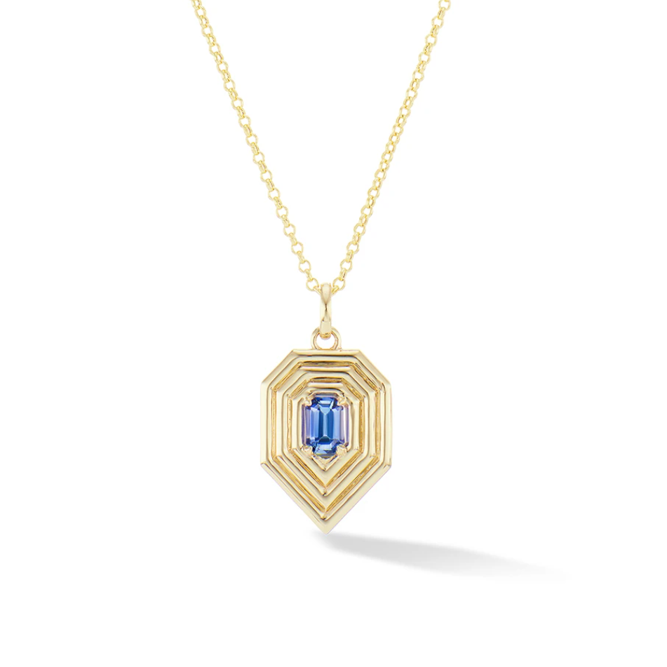 A gold pendant necklace featuring a geometric, stepped gold frame with a central blue emerald-cut gemstone, displayed on a clean white background with a soft shadow.