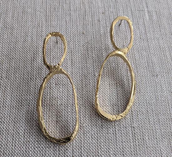 slightly angled view of the double oval post earrings on a textured beige background