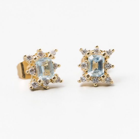 gold stud earrings with baguette shaped blue topaz and a halo of white cubic zirconia on a white background