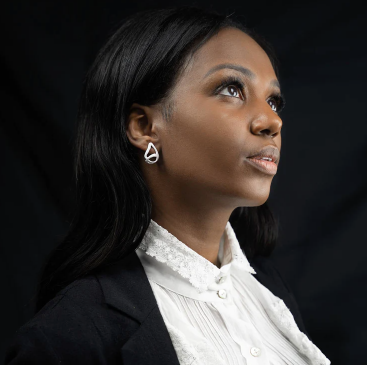 a model close up wearing the white small huggie earrings in a white top with black blazer on a black background