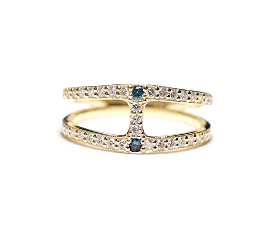 a 14k yellow gold split band with white diamond details and two teal tourmalines and a diamond bar down the middle of the ring, sitting one a white background