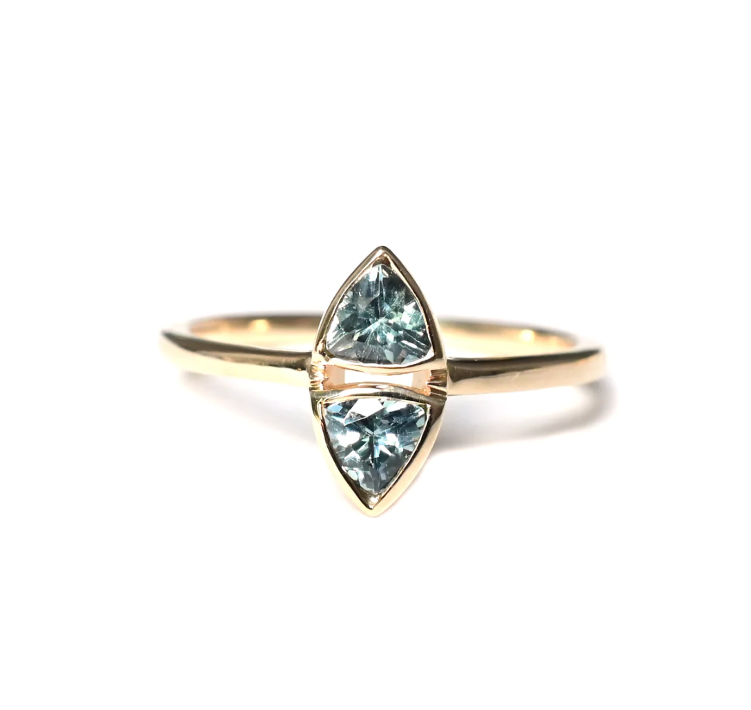 a 14k yellow gold solitaire ring featuring two trillion teal sapphires sitting one on top of the other with gold bezels, sitting on a white background
