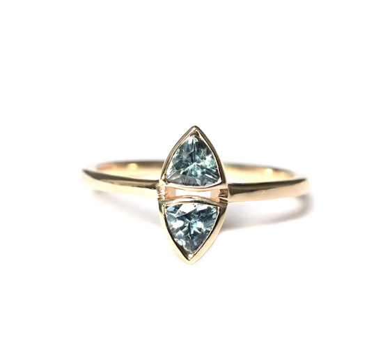 a 14k yellow gold solitaire ring featuring two trillion teal sapphires sitting one on top of the other with gold bezels, sitting on a white background