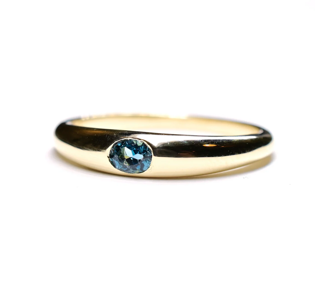 a classic domed gold band with an inset oval teal tourmaline sitting on a white background
