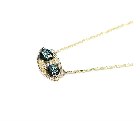 a marquise shaped pendant necklace with two round teal sapphire stones and milgrain details close up on a white background
