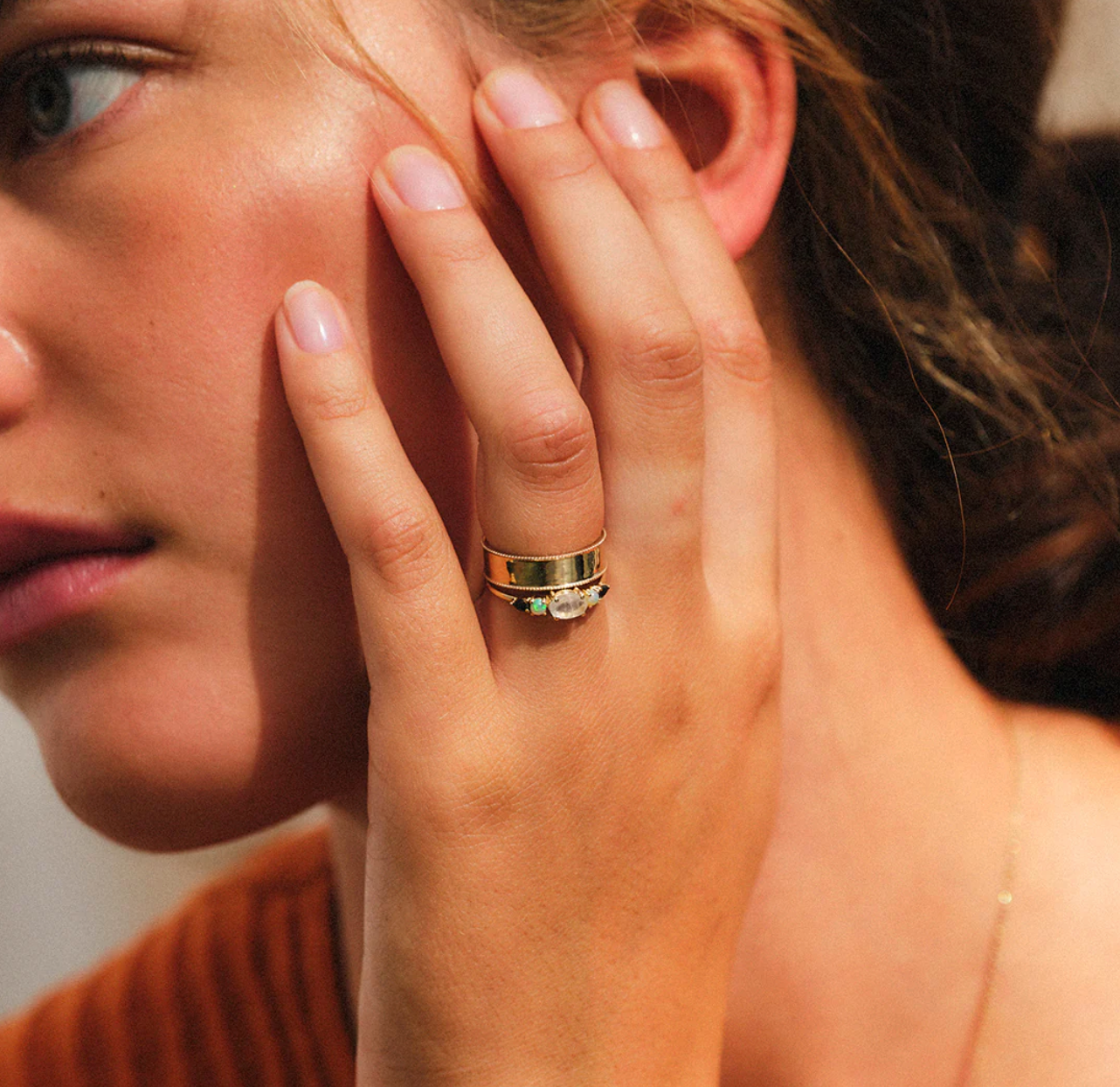 close up of a model wearing the multi gemstone claw set ring stacked with a simple gold band on her ring finger