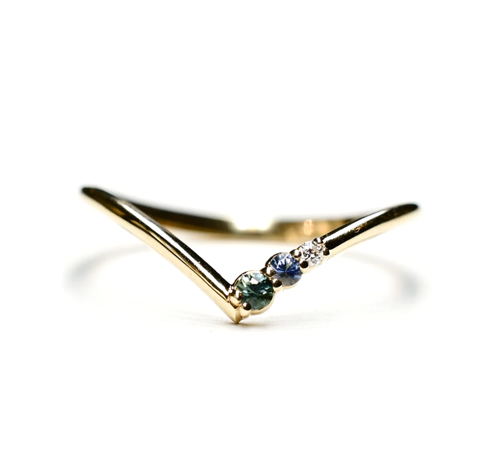 a yellow gold v band on a white back ground with an asymmetrical set teal tourmaline, blue tourmaline, and white diamond