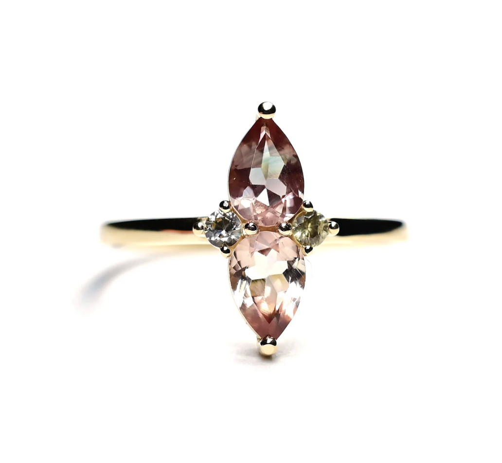 two pear shaped sunstones mirror each other on this 14k yellow gold ring sided by two round green sapphires
