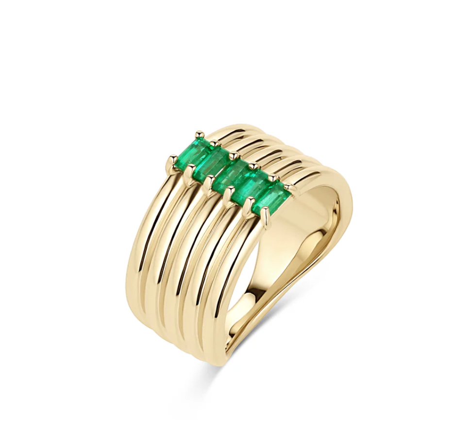a gold ring made to look like five bands stacked together with five baguette shaped emeralds in the center, angled on a white background