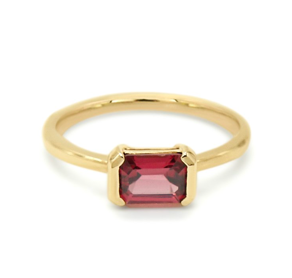 emerald cut rhodolite garnet is set in a half bezel solitaire on a white background