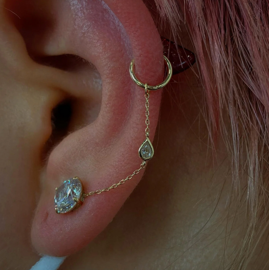 close up of a model wearing the teardrop chain on a clear gemstone stud and a gold hoop