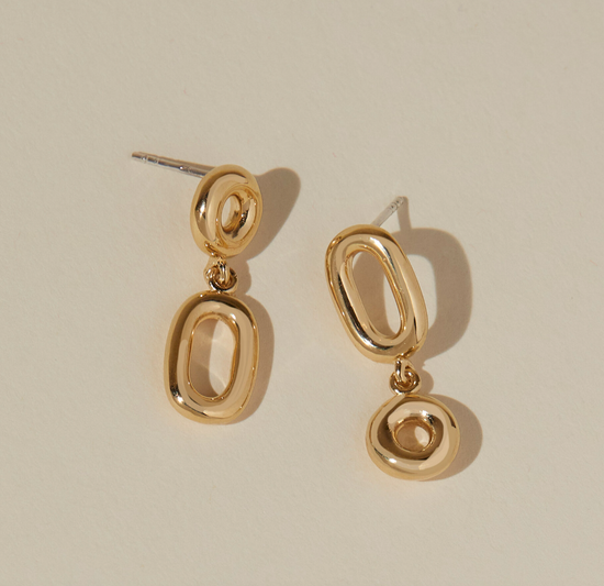 asymmetrical round and oval dangle earrings on beige background