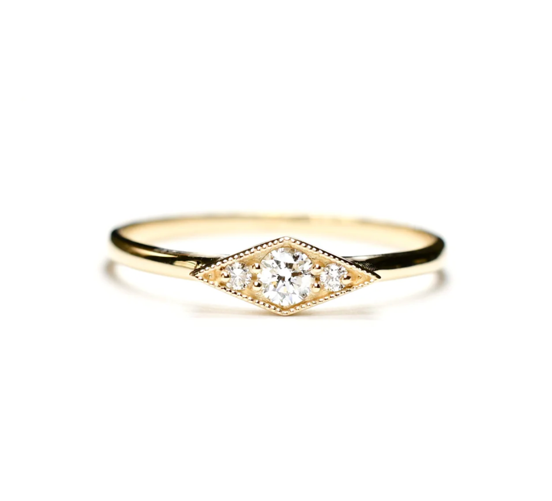14k yellow gold ring with three round white diamonds encased in a kite shaped gold mounting with milgrain detail on a white background