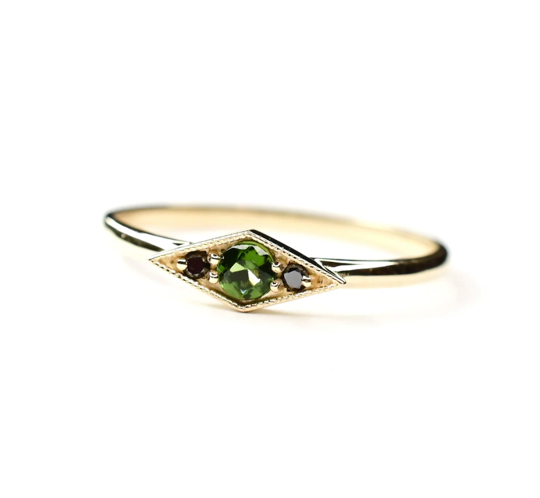 the shillay ring with a round bi-colored green tourmaline center and two round black diamonds on a white background