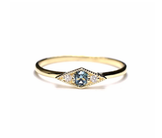 the shillay ring with a blue tourmaline center and two round white diamonds on a white background