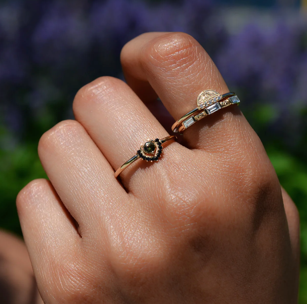 close up of a model wearing the glamis diamond ring on their pointer stacked with a baguette diamond band and another gemstone ring on their middle finger