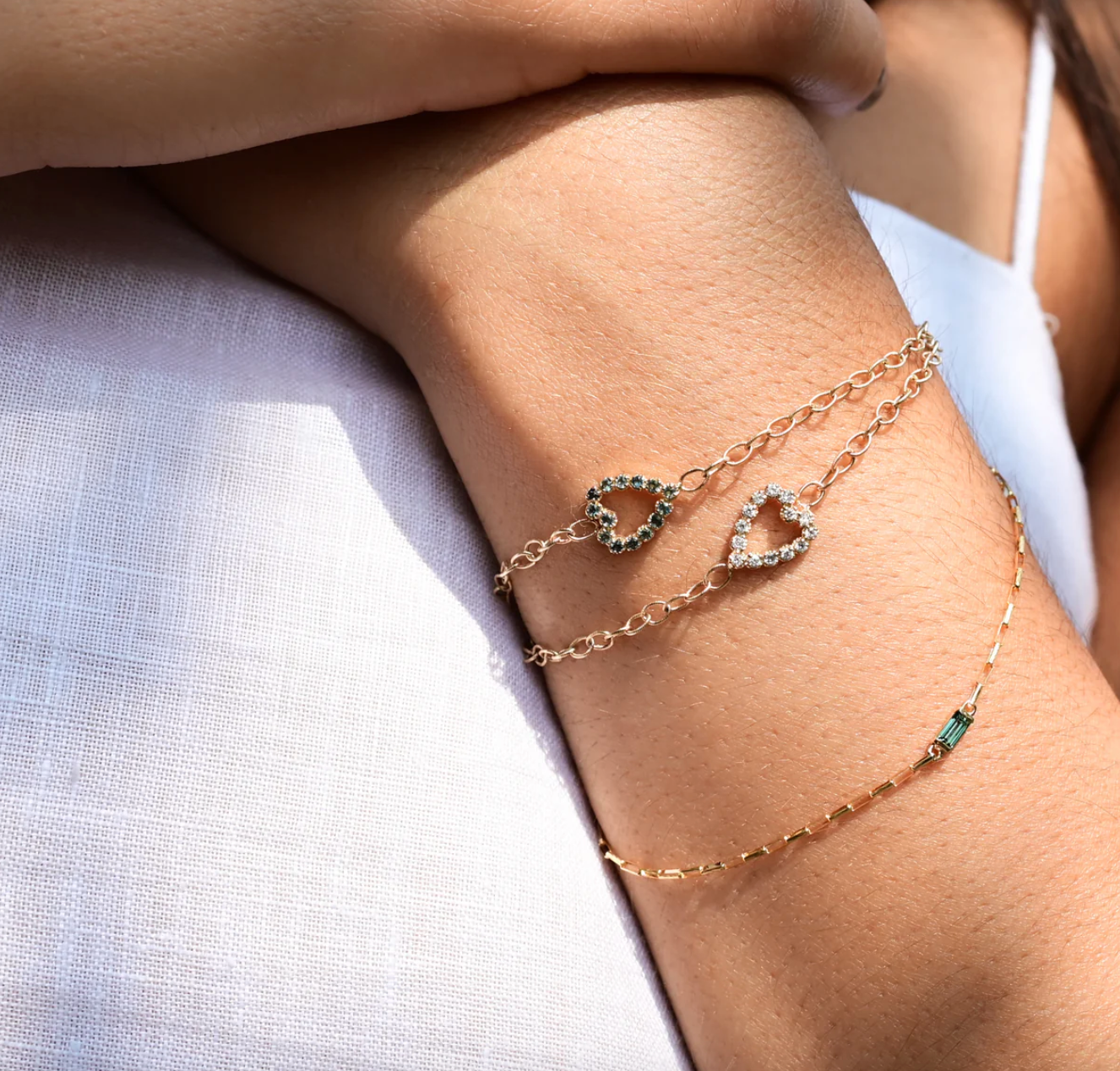 close up of a model wearing two gem heart bracelets and a chain bracelet 