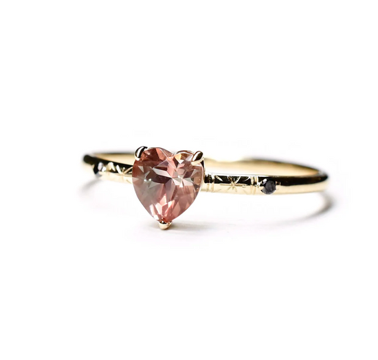 gold solitaire ring with a heart shaped sunstone center, engraved star details and two round black diamonds on a white background