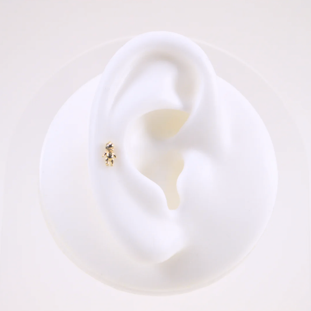 white silicone ear wearing the gold kewpie baby stud earring on a white background
