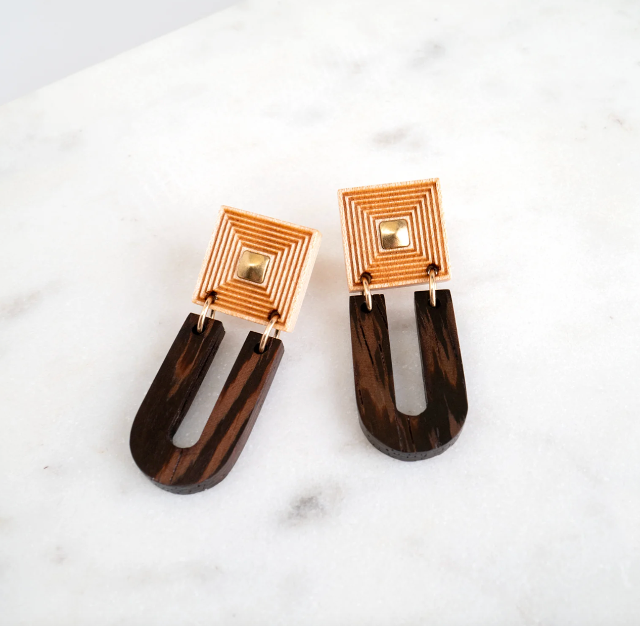 the fret earrings angled on a marble background