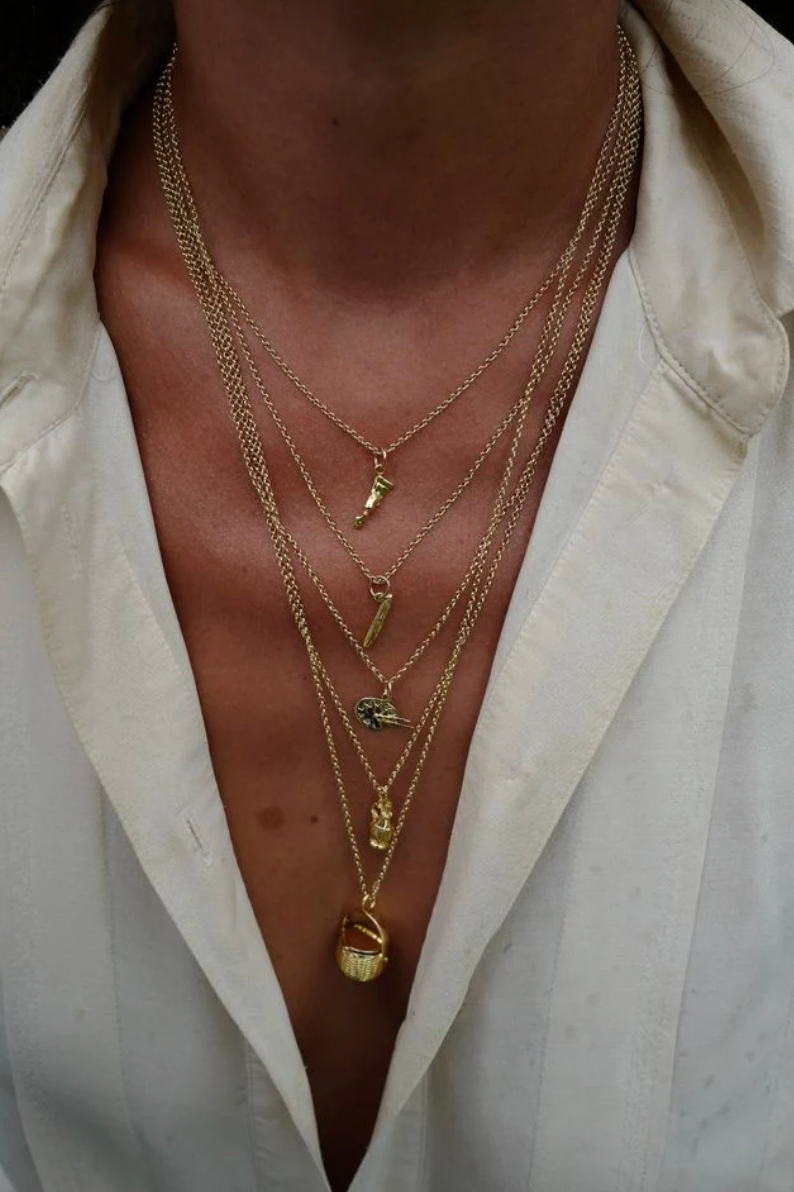 model wearing the birkin basket charm on a long gold chain layered with four other gold charm necklaces