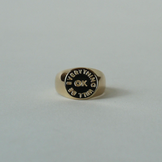 gold signet ring with the words "everything will be ok" engraved sitting on a grey background