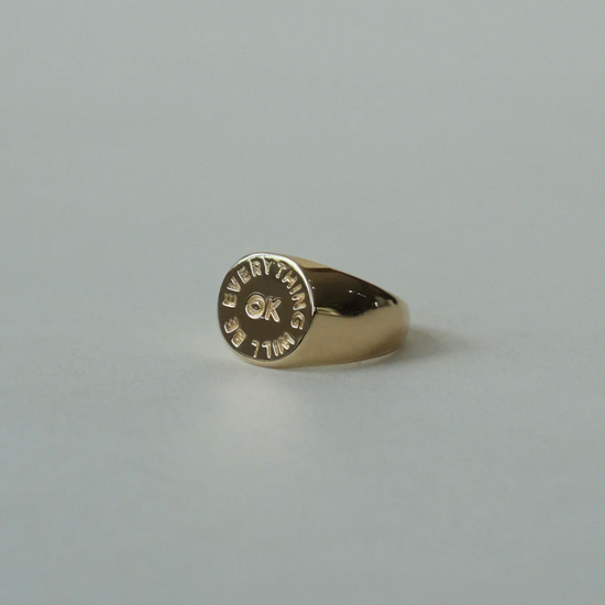 angled side view of the everything will be ok signet ring on a grey background