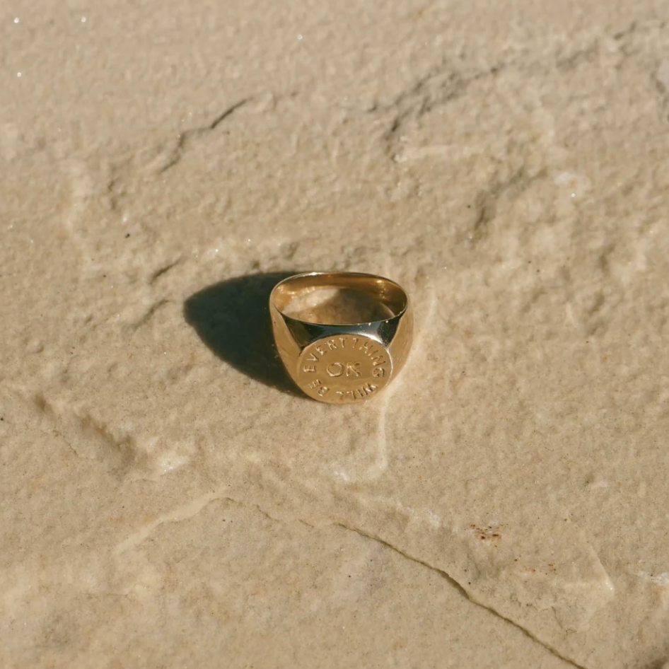 top view of the everything will be ok signet ring on a beige stone background