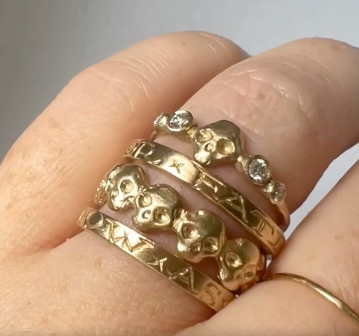 close up of a model wearing the skull eternity ring stacked with two engraved gold bands and a diamond and skull ring