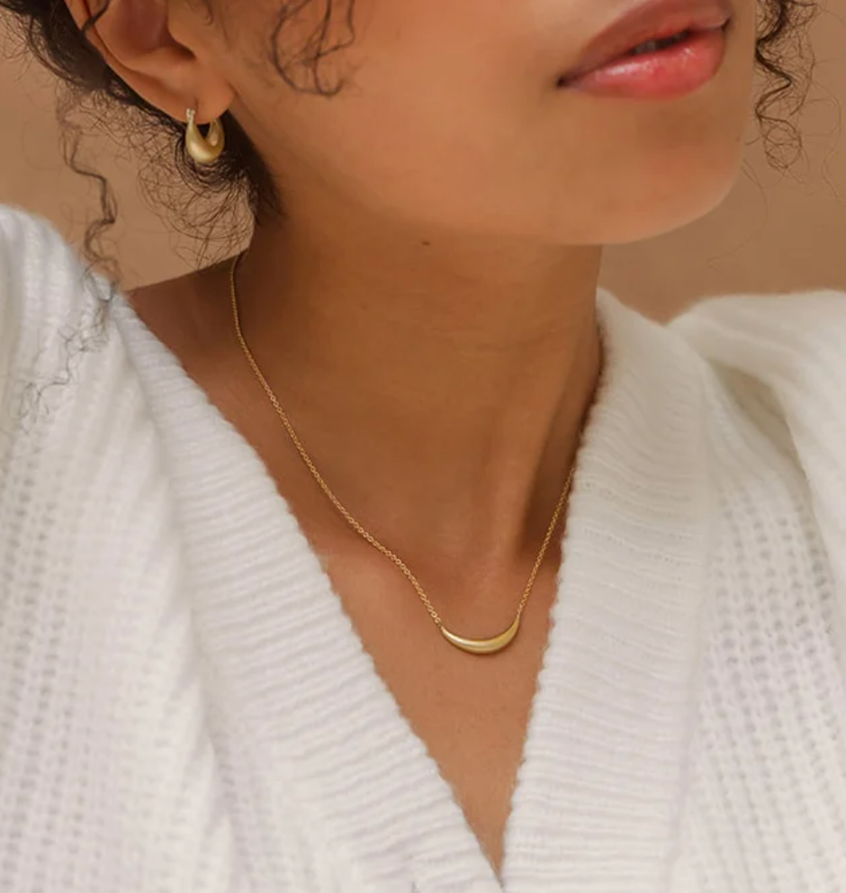 close up of a model wearing a curved pendant necklace