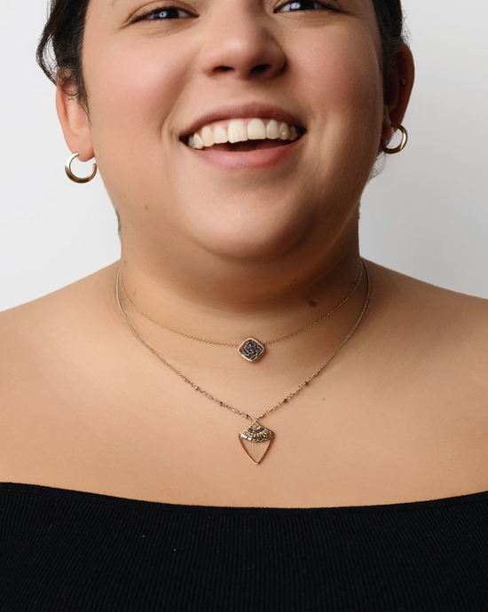 model wearing the dagger pendant layered with another beaded necklace and gold hoop earrings