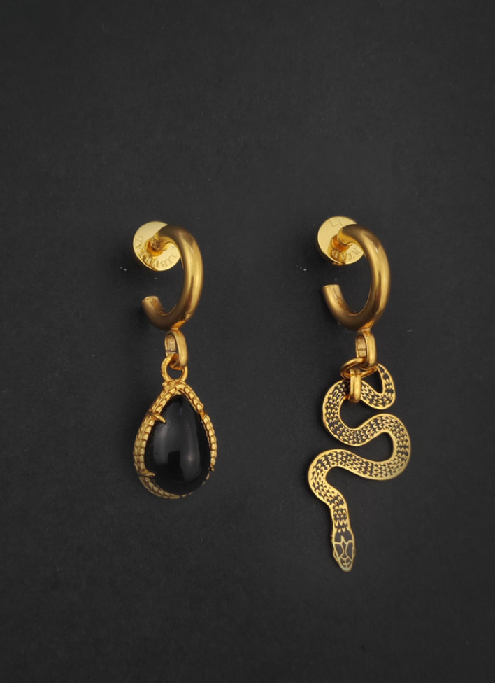 asymmetrical huggie earrings, one with a pear shaped onyx and one with a decorative snake on a black background