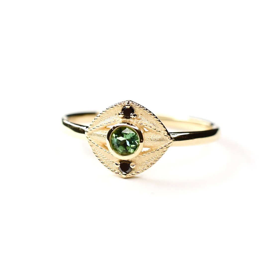 gold eye shaped ring with green tourmaline center stone and two black diamonds on white background