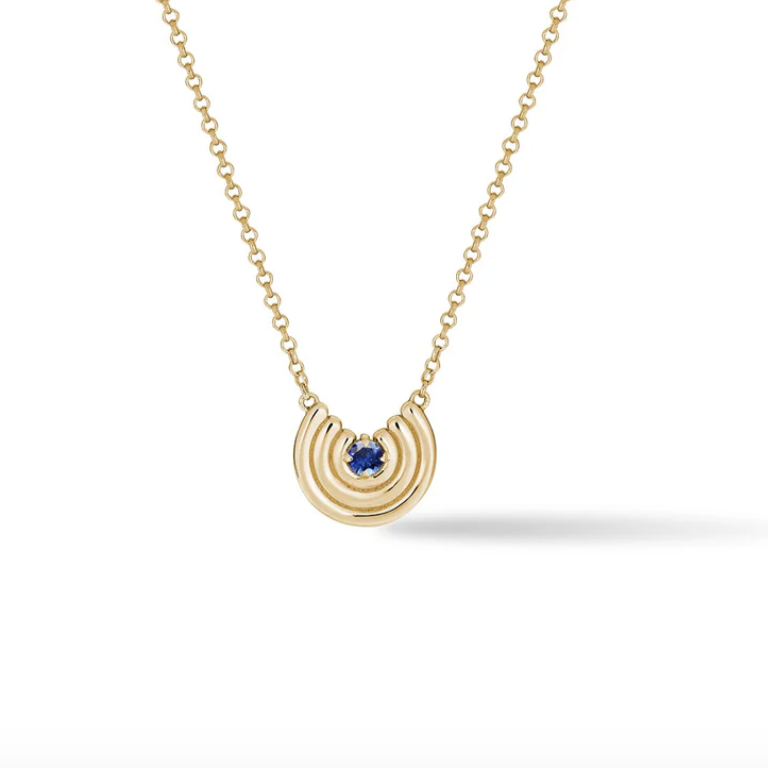 Gold necklace with a blue sapphire gemstone pendant on a white background