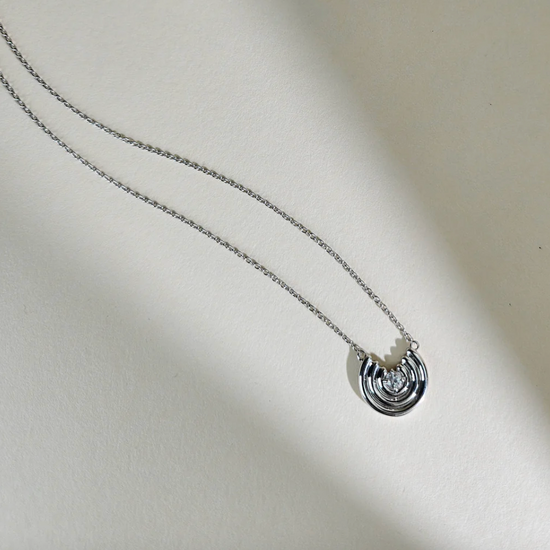 Silver necklace with a circular pendant on a light beige background