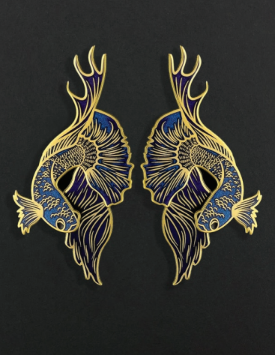 Pair of blue and gold betta fish-shaped earrings on a black background