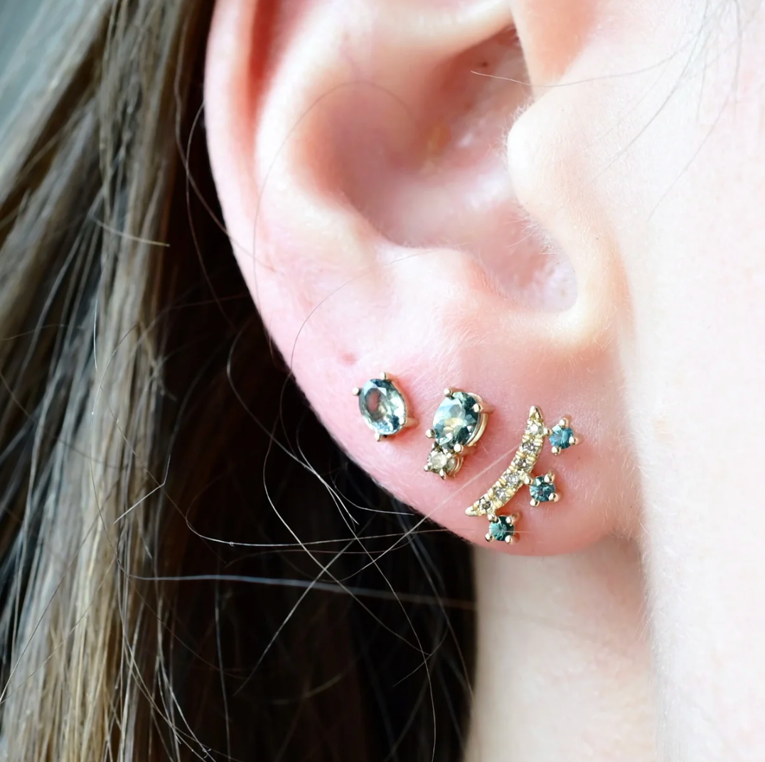Close-up of an ear wearing multiple earrings with gemstones.