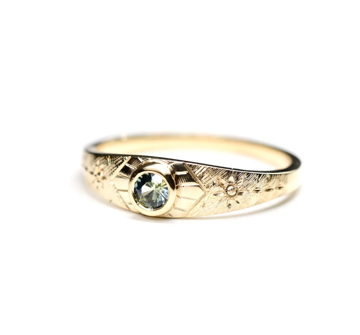 Gold ring with a sapphire and hand engraving on a white background