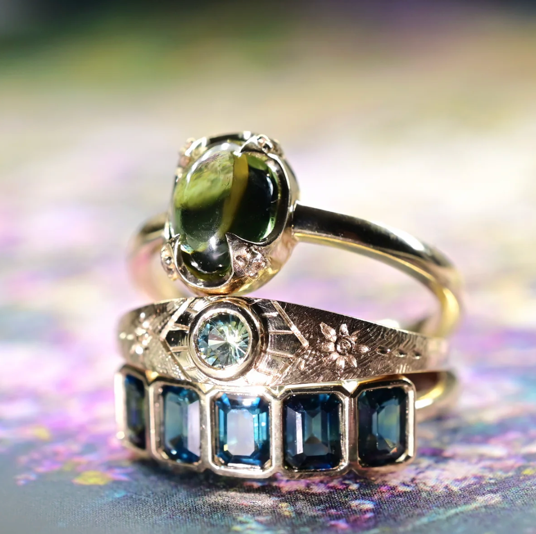 Three gold rings with gemstones on a colorful, blurred background