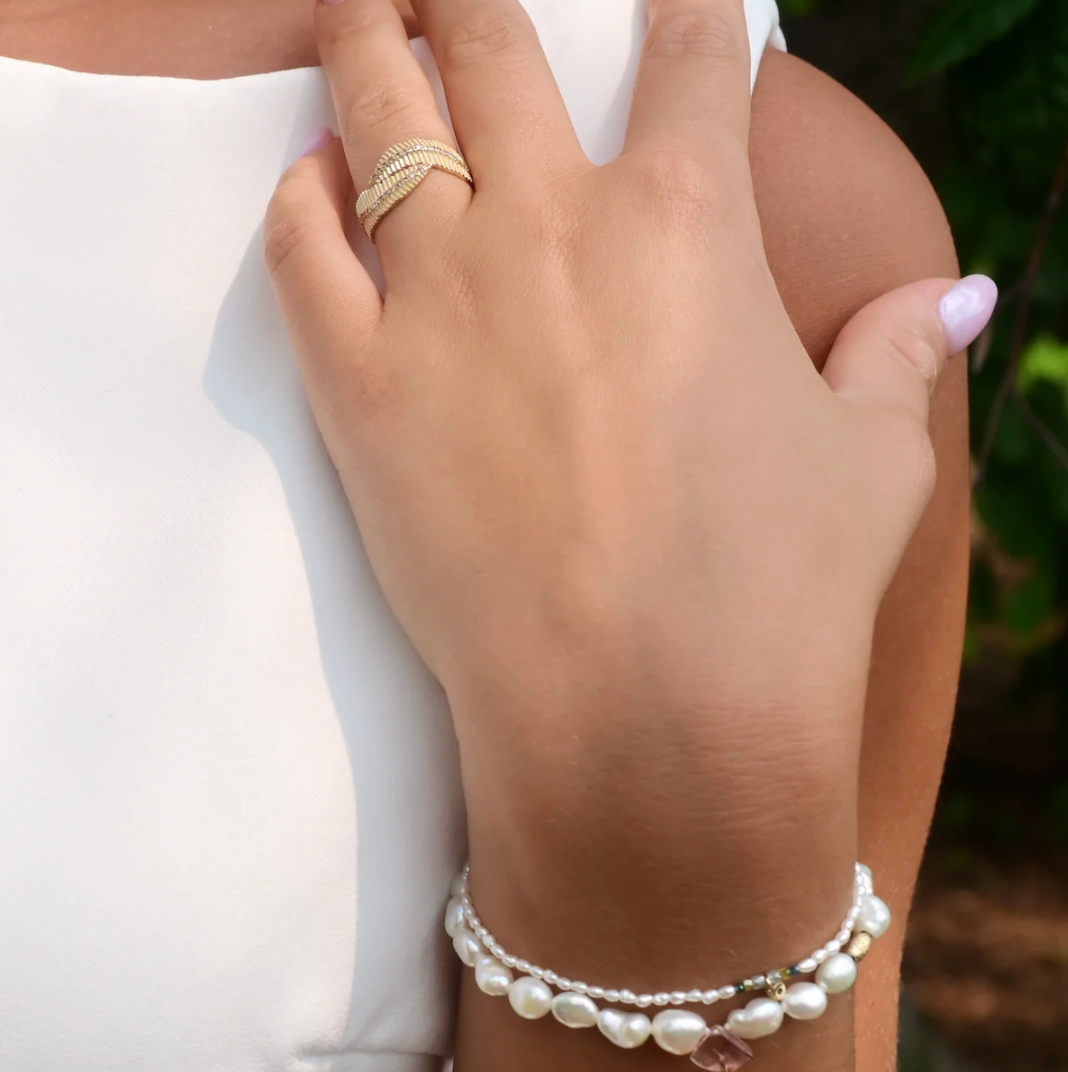 Hand wearing a gold ring and pearl bracelet with a blurred background
